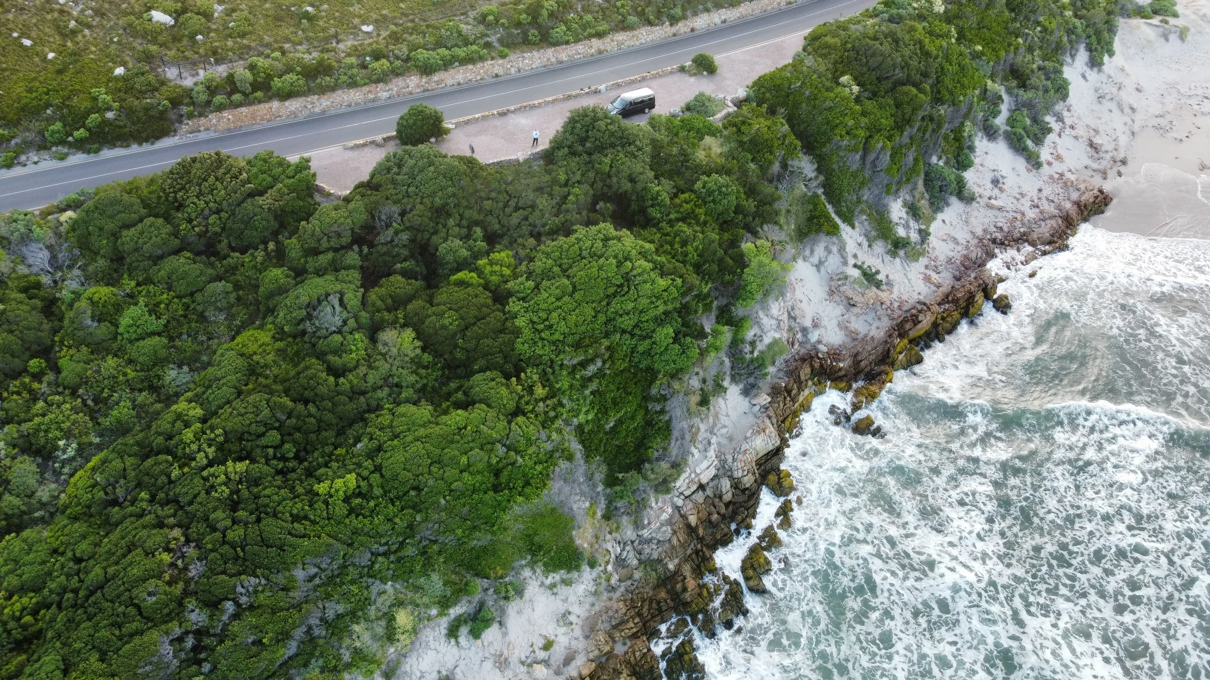 A coastal road running along a cliff above breaking waves, seen from the air